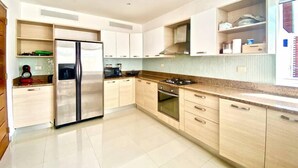 A modern kitchen with a stainless steel refrigerator, wooden cabinets, a gas stove, and a tiled backsplash. - Cap Cana PentHouse w/ terrace & private pool (Punta Cana)