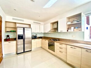 Una cocina moderna con un refrigerador de acero inoxidable, gabinetes de madera, una estufa a gas y una salpicadera de azulejos.