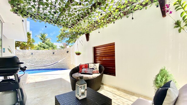 A patio area with a wicker sofa, a small table with a lantern, a hammock, and a view of a swimming pool. - Cap Cana PentHouse w/ terrace & private pool (Punta Cana)