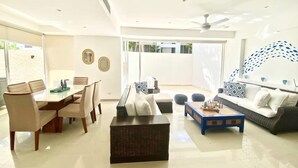 A modern living room with a dining area, a ceiling fan, and a large window. - Cap Cana PentHouse w/ terrace & private pool (Punta Cana)