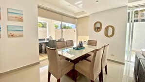 A modern dining area with a glass table, beige chairs, and a view of the outdoors. - Cap Cana PentHouse w/ terrace & private pool (Punta Cana)