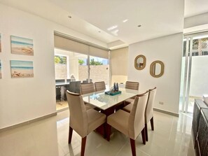 Un comedor moderno con una mesa de vidrio, sillas color beige y vistas al exterior.
