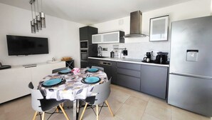A modern kitchen with a dining table, built-in appliances, and a flat-screen TV. - T3 sea view - beach & pool with all comforts (Linguizzetta)