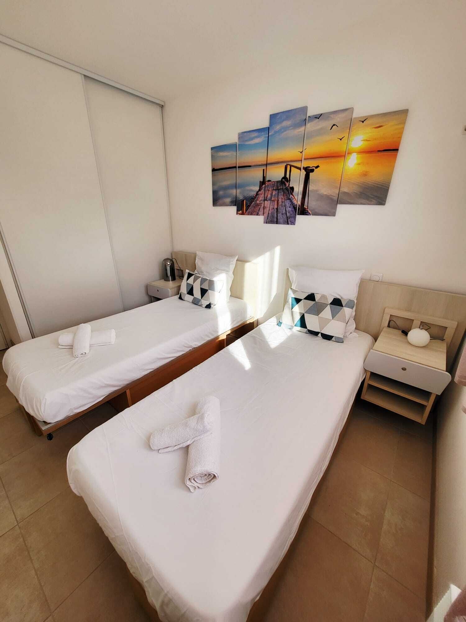 Une chambre d’hôtel avec deux lits, une table de chevet, un tableau accroché au mur et une fenêtre.