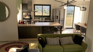 A modern living room with a green sofa, a grey sofa, and a round coffee table. There is a kitchen area with a large window, a refrigerator, and a dining table with chairs. - Vacation villa with private pool Lussan (near Uzès) (Lussan)