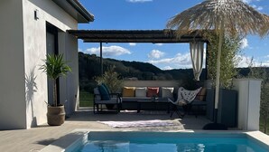 A swimming pool with clear water, a covered seating area with cushions, and a view of hills in the background. - Vacation villa with private pool Lussan (near Uzès) (Lussan)