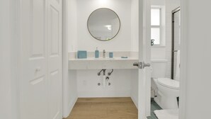 A bathroom with a white door, a round mirror, a white sink with blue soap dispensers, and a white toilet. - Boutique Hotel 2 double beds with POOL, LOCATION! 1 block to BEACH/Restaurants (Deerfield Beach)