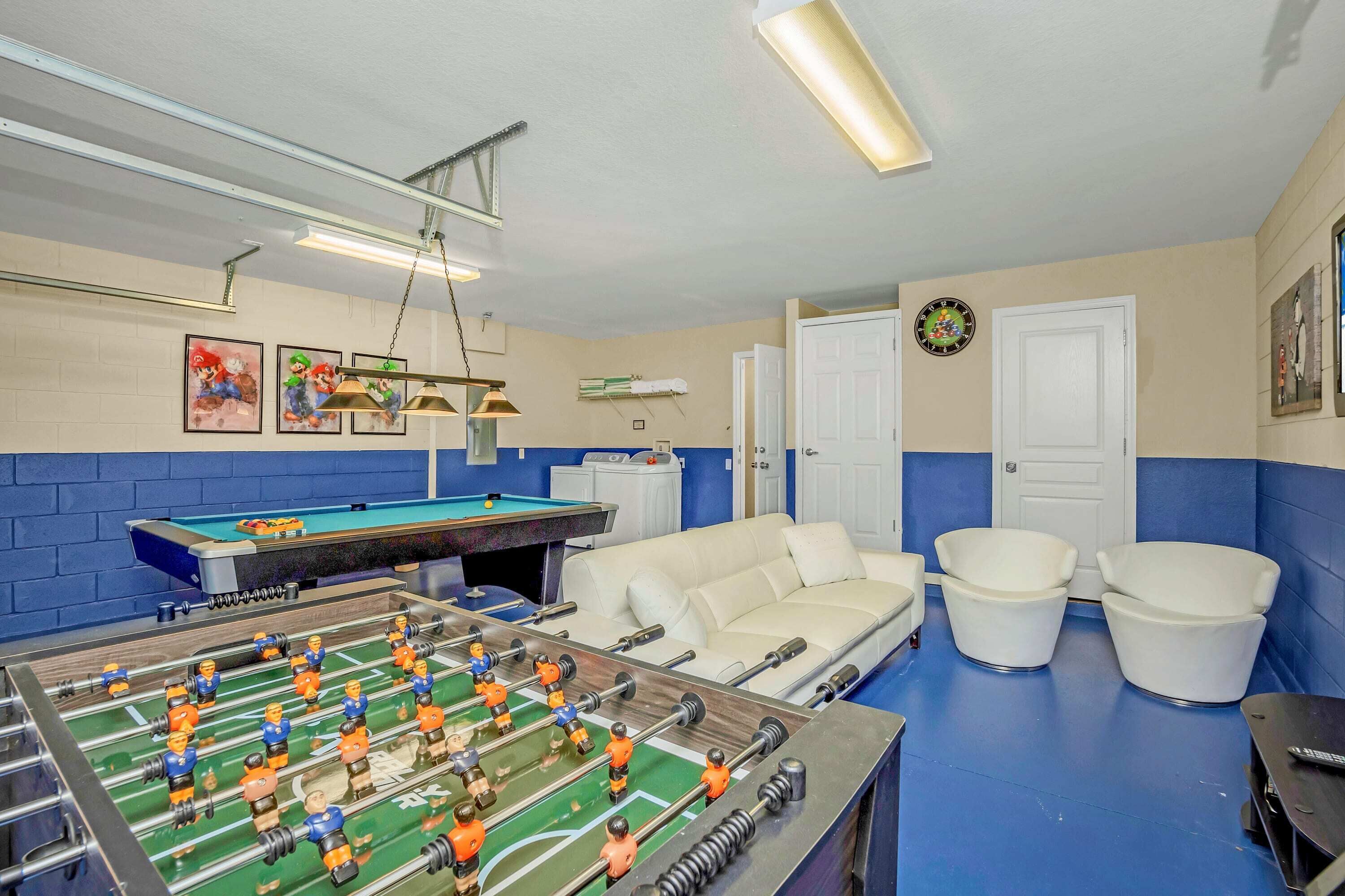 Una habitación con mesa de futbolín, mesa de billar, un sofá blanco y dos sillones blancos.