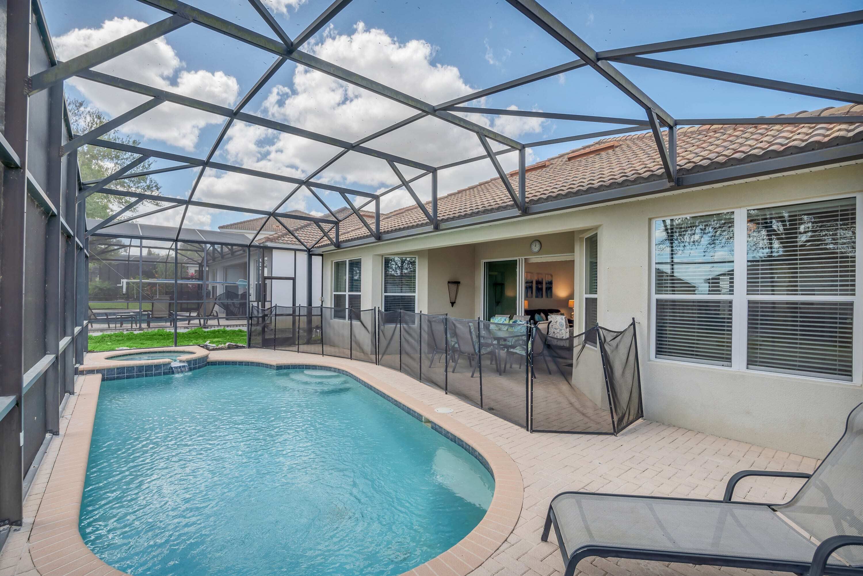 A covered swimming pool with a patio area, a fenced deck, and a view of a building with windows and a door.