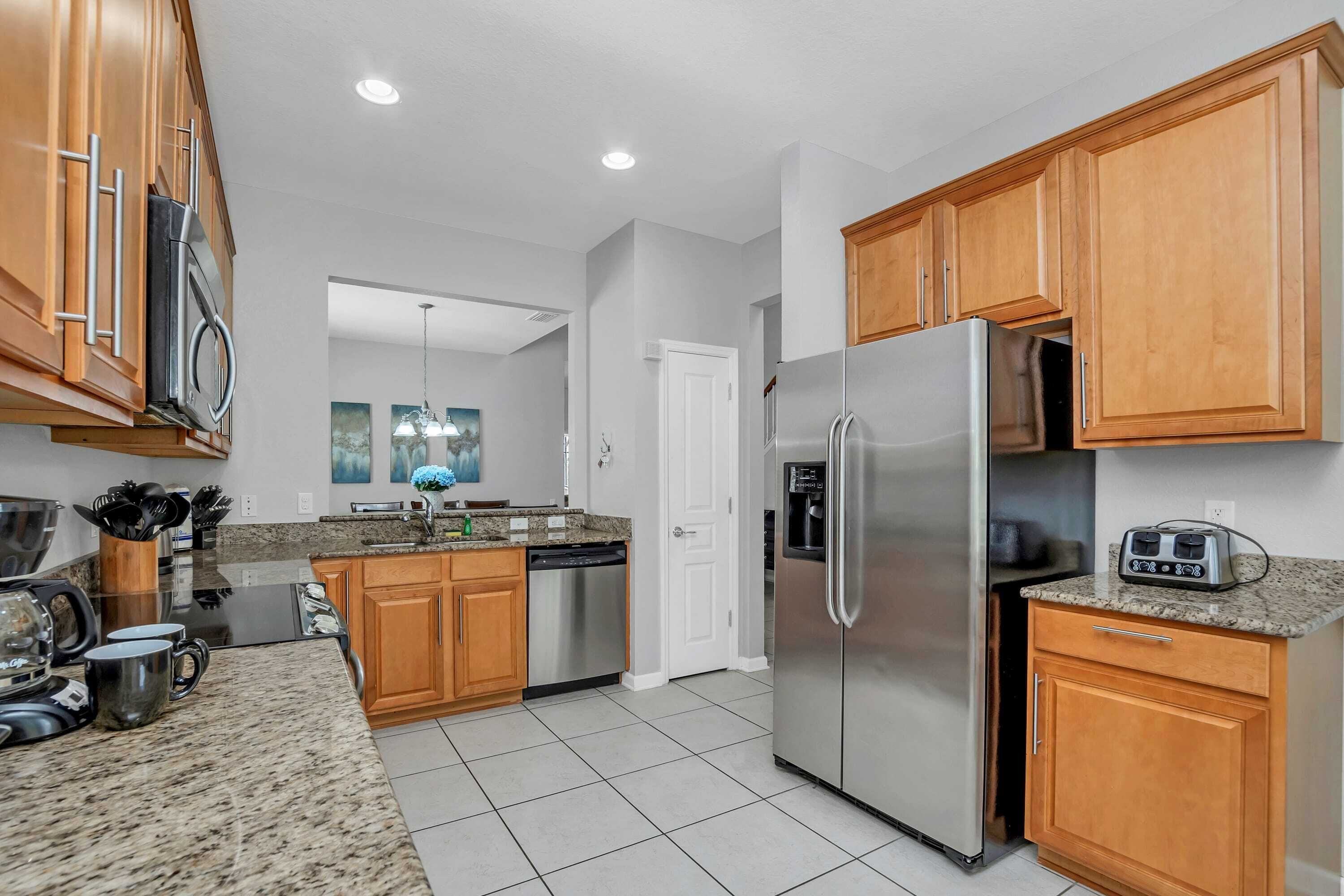 A modern kitchen with granite countertops, stainless steel appliances, wooden cabinets, and a dishwasher.