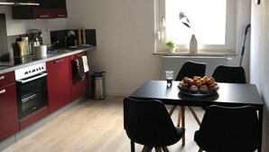 A modern kitchen with red cabinets, a dining table with black chairs, and a window with a view of the sky. - Ferienzimmer (Zwickau)