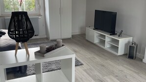 A modern living room with a white wardrobe, a TV on a white stand, and a black floor lamp. - Ferienzimmer (Zwickau)