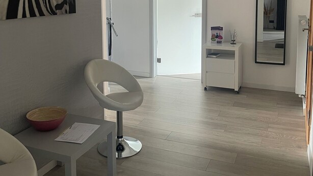 A modern, minimalist room with a zebra print artwork, a white desk with a bowl, a chair, a standing lamp, a mirror, and a door leading to another room. - Ferienzimmer (Zwickau)