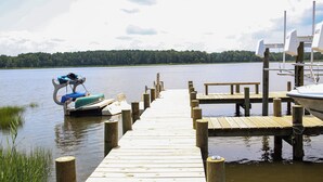 Eine Holzstege erstreckt sich über einen stillen See, mit einem Boot am rechten und einem Kajak am linken Ende.