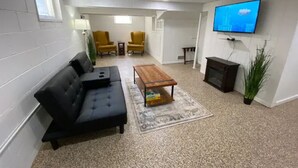 Un soggiorno con un divano nero, un tavolino in legno e una TV a parete.
