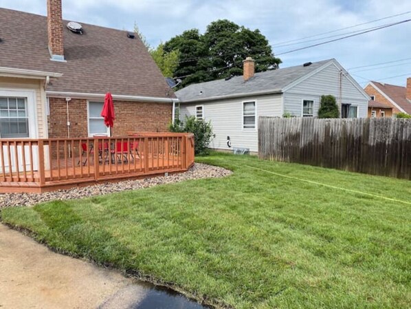 A residential backyard with a wooden deck, a lawn, and a wooden fence.