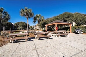 Enjoy al fresco dining under the shade of a pavilion, surrounded by lush trees and a barbecue grill.