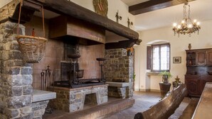 A stone fireplace with a bench, wooden beams, and a chandelier. - Villa Radda by MMega (Gaiole In Chianti)