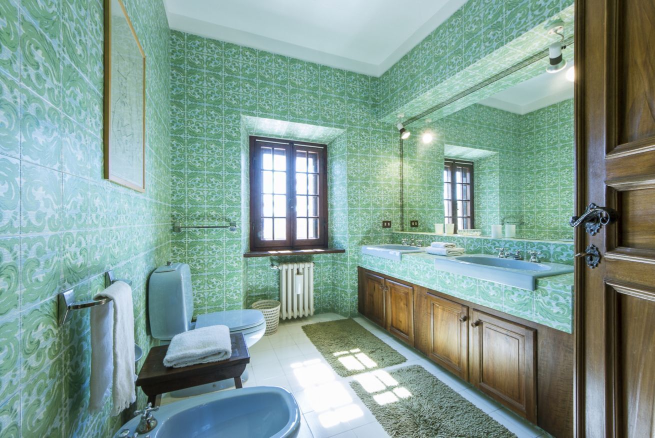 Um banheiro com azulejos estampados em tons de verde, uma banheira, uma pia e uma janela.