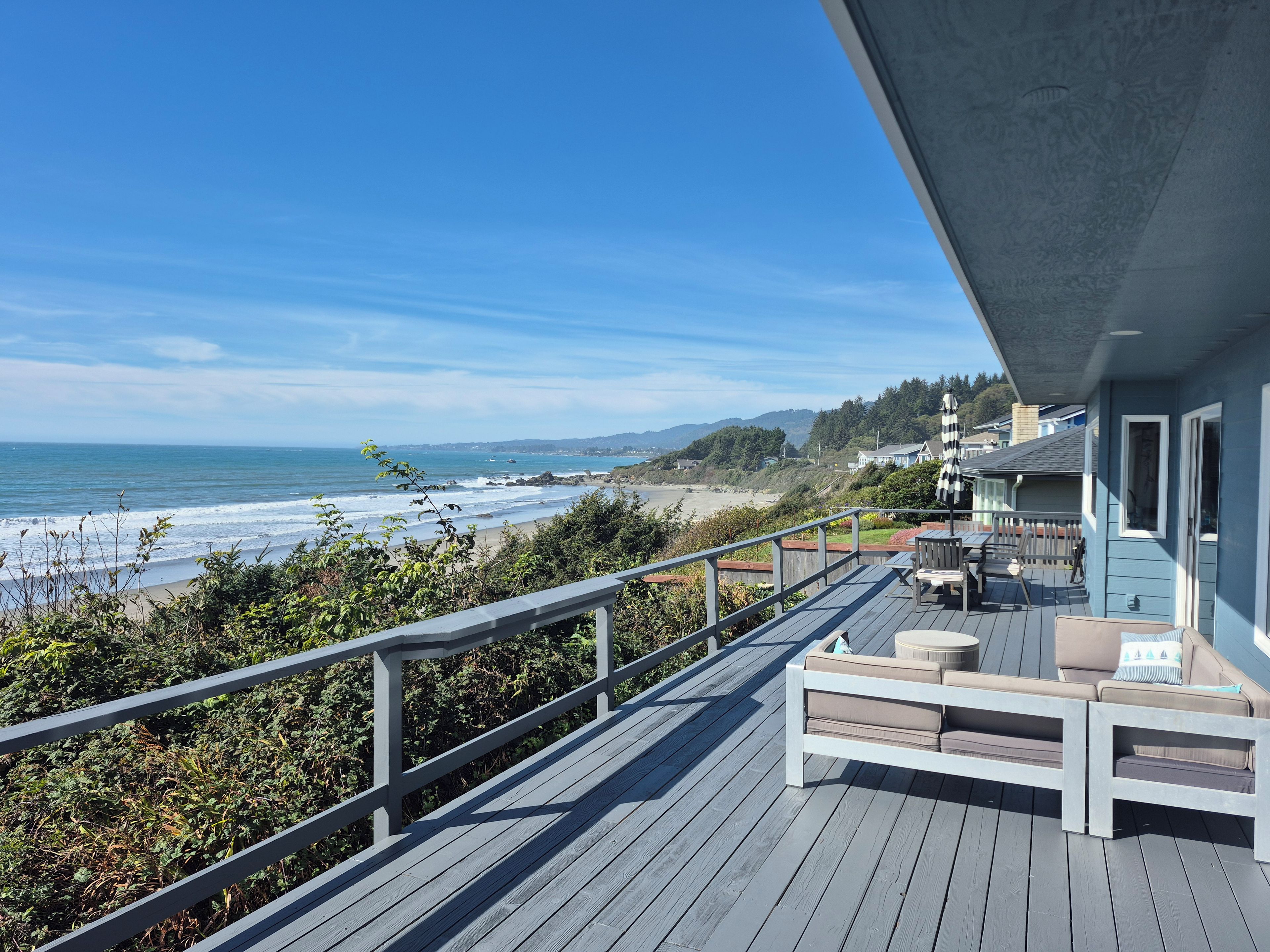 A wooden deck with outdoor furniture overlooking a beach and ocean.