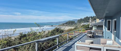 A wooden deck with outdoor furniture overlooking a beach and ocean.