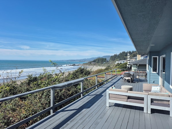 A wooden deck with outdoor furniture overlooking a beach and ocean.