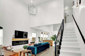 Amplia sala de estar con un televisor de pantalla plana grande, un sofá azul y una escalera con peldaños estampados.
