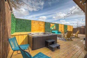 A wooden deck with a hot tub, seating area, and a wall with a green mosaic. - Hottub-Deck-Firepit-Cornhole! (Fredericksburg)