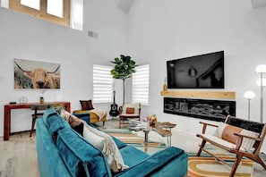 Un salón amplio con un sofá azul grande, una mesa de centro de madera y una chimenea moderna.
