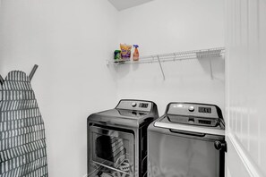 A laundry room with two washing machines, a drying rack, and a shelf with laundry detergent.