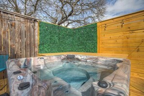 Un jacuzzi en un área de terraza de madera con un muro de seto artificial verde.