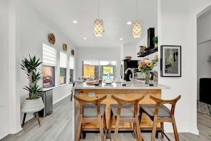 Una cocina moderna con una isla central, sillas de madera, luces colgantes y vistas al exterior.