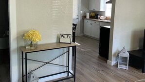 A modern living room with a wooden floor, a console table with a vase of flowers, a Wi-Fi sign, and a view into the kitchen through an archway. - Hidden Gem-10 minutes to DT Chatt! Perfect for teleworkers, small families, etc. (Rossville)