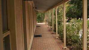 A covered walkway with brick flooring, columns, and a row of windows on one side. - The Blush 3 - Style in the vines (Penwortham)