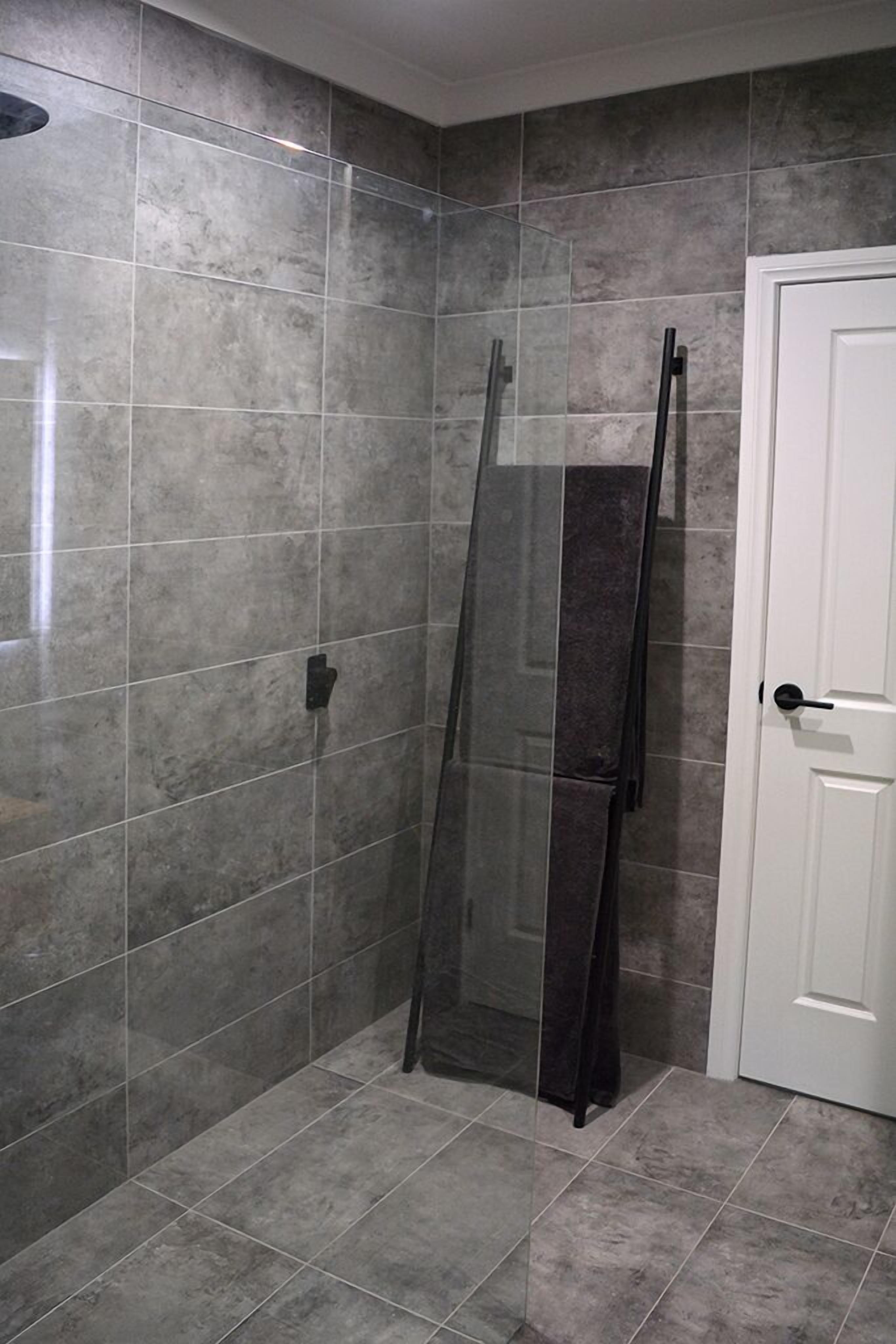 Une salle de bain avec des carreaux gris, une douche en verre et une porte blanche.