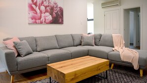 A modern living room with a grey sectional sofa, a wooden coffee table, and a large floral artwork on the wall. - The Blush 3 - Style in the vines (Penwortham)