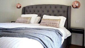 A neatly made bed with a grey headboard, two pillows, and a grey blanket. - The Blush 3 - Style in the vines (Penwortham)