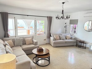 A living room with a sofa, a round coffee table, a lamp, a chandelier, and a view through large windows.
