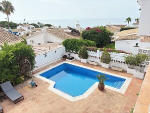 Una piscina en la azotea con vistas al mar, rodeada de muros blancos y vegetación.