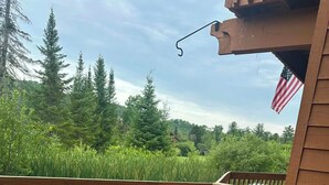 A wooden deck with red chairs and a table, overlooking a grassy area with trees. - Newly decorated 2 BR 2 bath Sleeps 6 outdoor pool, close to Torch Lake, wifi (Mancelona)