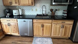 A kitchen with wooden cabinets, a stainless steel microwave, a dishwasher, and a tiled backsplash. - Newly decorated 2 BR 2 bath Sleeps 6 outdoor pool, close to Torch Lake, wifi (Mancelona)