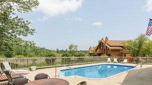 A pool area with a wooden deck, lounge chairs, and a flag. - Newly decorated 2 BR 2 bath Sleeps 6 outdoor pool, close to Torch Lake, wifi (Mancelona)