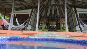 Ein Poolbereich mit glatter, blauer Wasseroberfläche, einer Holzkonstruktion darüber und einer Hängematte zwischen zwei Pfosten.