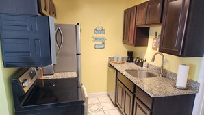 A compact kitchen with dark wooden cabinets, a stainless steel refrigerator, a black stove, and a granite countertop.