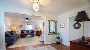 Ein Wohnzimmer mit einer Couch, einem Couchtisch und Dekoration. Es gibt einen Deckenventilator, eine Kristallleuchter und einen Spiegel an der Wand.
