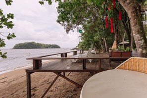 Relax on the beachside deck with lounge chairs and a table, overlooking the calm sea and a distant island.