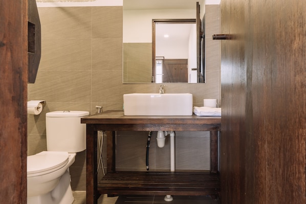 Un baño con tocador de madera, lavamanos blanco y un inodoro.