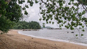 A beach with a sandy shore, calm water, and dense greenery in the background. - Roxy Telok Serabang (Lundu)