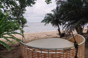 A beach view with a wicker chair and a hammock.