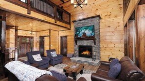 Ein gemütliches Blockhaus-Interieur mit Kamin aus Stein, Ledersofas und Holzbalkendecke.